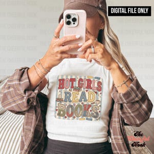 Pode incluir: Camiseta branca com o texto "HOT GIRLS READ BOOKS" em um design retrô colorido. A camisa apresenta uma pilha de livros, corações e um gráfico de xícara de café. As palavras são em vermelho, azul, amarelo e verde. As palavras estão em um quadrado.