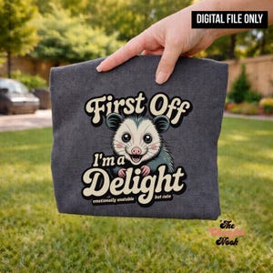 May include: Dark gray t-shirt featuring a cartoon opossum with the text "First Off I'm a Delight" and "emotionally unstable but cute". The image is a digital file.