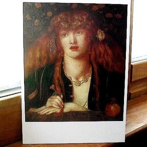 May include: A framed print of a Renaissance-style portrait of a woman with long, flowing red hair. She wears a gold necklace and a dark green and black garment. An apple is visible in the lower right corner. The artwork has a vintage aesthetic.