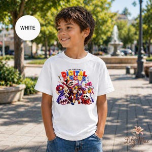 K&ouml;nnte beinhalten: Ein wei&szlig;es T-Shirt mit einem farbenfrohen Grafikdesign von "The Amazing Digital Circus". Das Design zeigt verschiedene Cartoon-Charaktere und den Text "THE AMAZING DIGITAL CIRCUS". Das T-Shirt wird von einer Person in blauen Jeans getragen.