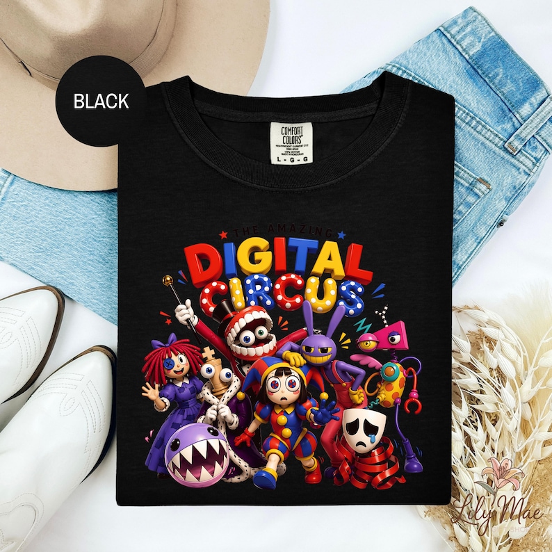 K&ouml;nnte beinhalten: Schwarzes T-Shirt mit einem farbenfrohen Grafikdesign von Cartoon-Charakteren und dem Text "DIGITAL CIRCUS" in Rot, Gelb und Blau. Das T-Shirt hat einen Rundhalsausschnitt und ein "Comfort Colors"-Etikett.