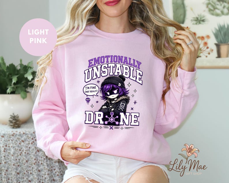 May include: Light pink sweatshirt with the text "Emotionally Unstable Drone" and a cartoon character graphic. The graphic includes the phrase "I'm fine (not really)". The sweatshirt is a crew neck style.