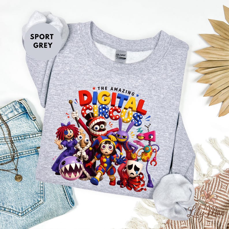 K&ouml;nnte beinhalten: Sportgraues Sweatshirt mit einem farbenfrohen Grafikdesign von Charakteren aus "The Amazing Digital Circus". Das Design zeigt Cartoonfiguren in leuchtenden Farben mit dem Text "THE AMAZING DIGITAL CIRCUS" in mehrfarbigen Buchstaben.