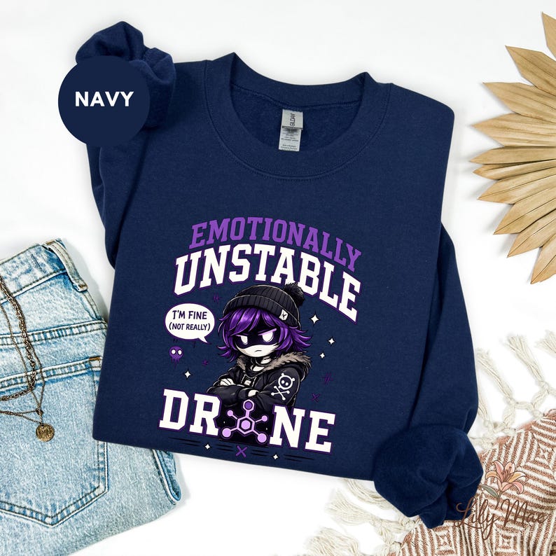 May include: Navy blue sweatshirt with the text "Emotionally Unstable Drone" and a graphic of an anime-style character. The character has purple hair and is wearing a black beanie and jacket. The text "I'm fine (not really)" is also included.