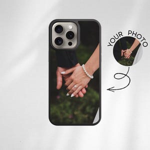 Könnte beinhalten: Schwarze Handyhülle mit einem Foto von zwei Händen, die sich halten, einem Perlenarmband und einem Ring. Die Hülle hat einen schwarzen Rand und ein kleines rundes Bild mit den Worten "YOUR PHOTO".