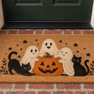 May include: A rectangular tan coir doormat featuring a printed illustration of three white ghosts and two black cats gathered around a central orange jack-o'-lantern. The design includes small black stars scattered across the top portion.