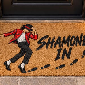 Puede incluir: Un felpudo rectangular de fibra de coco color canela con una ilustración gráfica de un bailarín con chaqueta roja, pantalones negros y sombrero fedora negro. El texto SHAMONE IN está impreso en negro junto a huellas de pasos negras.
