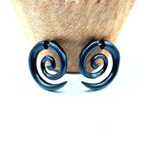 May include: A pair of dark blue spiral-shaped earrings. The earrings have a smooth, glossy finish and a curved design. The earrings are displayed against a light brown background.