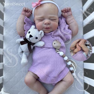 Może przedstawiać: Śpiące dziecko w lawendowym body i białej opasce z różowym kwiatkiem. Mały, szydełkowy miś z brązową kokardą i drewniany klips do smoczka leżą obok dziecka. Tekst "NamiSweet" znajduje się w lewym górnym rogu.