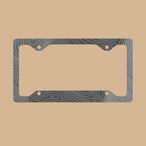 Op de afbeelding: Een rechthoekig kentekenplaathouder met een donkergrijs oppervlak en een wit topografisch patroon van hoogtelijnen. Het frame is voorzien van vier ronde montagegaten in de hoeken om de plaat aan een voertuig te bevestigen.