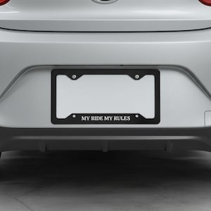 May include: A black license plate frame with the text "MY RIDE MY RULES" in white lettering. The frame is mounted on a silver vehicle. The license plate area is blank.