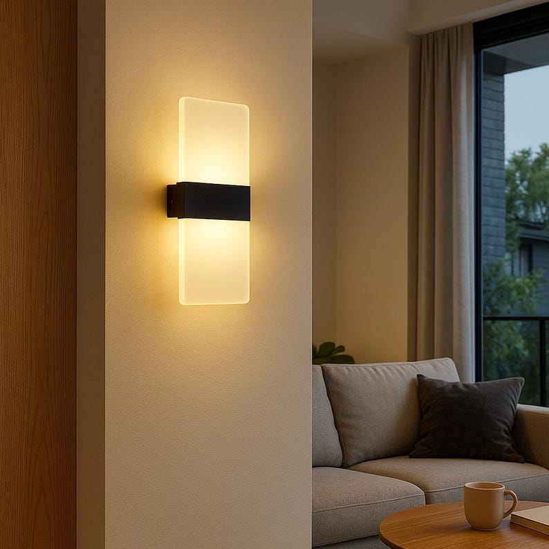 K&ouml;nnte beinhalten: Moderne Wandleuchte mit rechteckigem, mattiertem Glasschirm. Die Leuchte hat ein schwarzes Band in der Mitte und ist an einer beigen Wand befestigt. Die Leuchte strahlt ein warmes Licht aus, das sich f&uuml;r die Innenbeleuchtung eignet.
