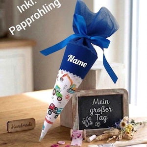 Könnte beinhalten: Eine blaue und weiße Schultüte mit einem Muster von Baufahrzeugen. Die Tüte ist mit einem blauen Band gebunden und trägt den Schriftzug "Name". Eine kleine Tafel mit der Aufschrift "Mein großer Tag" ist ebenfalls vorhanden.