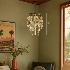 May include: A decorative chandelier with a circular frame and hanging, iridescent, shell-like discs. The chandelier is approximately 11 inches in length. The fixture hangs from a chain and is suspended from a dark ceiling. The room has a vintage aesthetic.