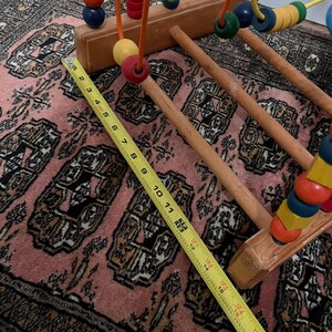 May include: Wooden bead maze toy with colorful beads on wire tracks. The wooden base is light brown, and the beads are various colors. A yellow measuring tape shows the toy is approximately 18 inches long.
