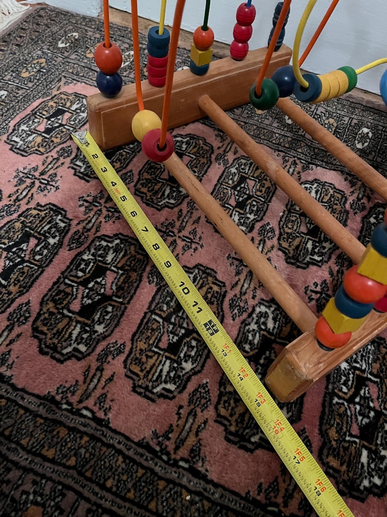 May include: Wooden bead maze toy with colorful beads on wire tracks. The wooden base is light brown, and the beads are various colors. A yellow measuring tape shows the toy is approximately 18 inches long.