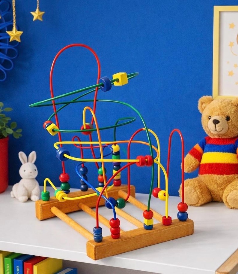 May include: A wooden bead maze toy with colorful wires and beads. The toy features red, yellow, green, and blue wires with matching beads. A plush teddy bear and a white bunny are in the background.