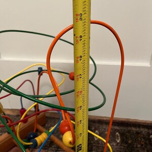 May include: A colorful wooden bead maze toy with a measuring tape showing a height of approximately 21 inches. The maze features orange, green, yellow, and blue wires with matching beads. The toy is designed for children.