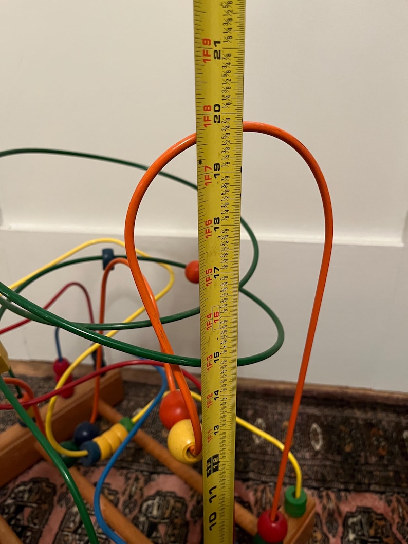May include: A colorful wooden bead maze toy with a measuring tape showing a height of approximately 21 inches. The maze features orange, green, yellow, and blue wires with matching beads. The toy is designed for children.