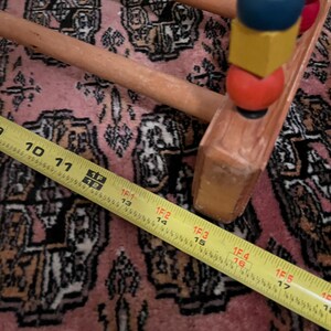May include: Wooden abacus with colorful beads, including red, blue, and yellow. A yellow measuring tape shows a length of 16 inches. The abacus is on a pink patterned rug.