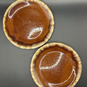 May include: Two brown ceramic plates with a textured, speckled rim. The plates have a glossy, smooth surface and a rich, warm brown color. The rims are a lighter shade of brown, creating a contrasting border.