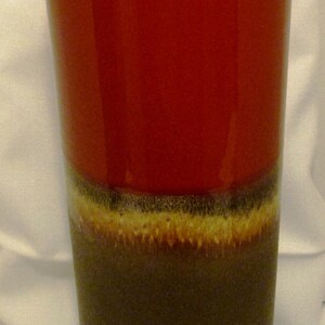 May include: A red and brown ceramic vase with a glazed finish. The vase has a wide mouth and a narrow base.