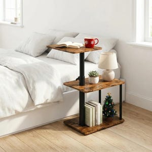 May include: A three-tiered side table with a rustic wood-look finish and black metal supports. The top shelf holds a red mug with snowflake designs, and an open book. The bottom shelf displays books and a small Christmas tree.