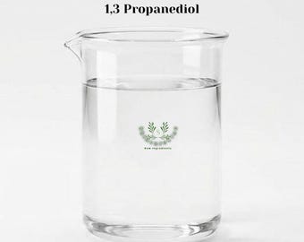 May include: A clear glass beaker filled with a transparent liquid, labelled 1,3 Propanediol at the top. A small circular logo featuring green leaves and the letter S is centred on the front of the beaker, with the text Raw Ingredients below it.