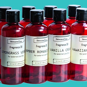 May include: A collection of red-tinted fragrance oil bottles with black caps and white labels. The labels display the brand name "Skincare Clue" and various scents like "Lemongrass Verbena" and "Vanilla Cream". The bottles are for external use only.