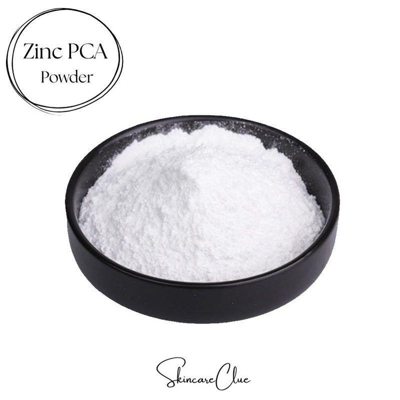 May include: A small black bowl filled with fine white Zinc PCA Powder. The text Zinc PCA Powder is enclosed in a circular line at the top left, and the text Skincare Clue is written in a cursive script at the bottom center of the image.