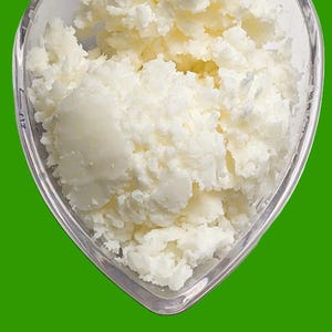 Op de afbeelding: Een heldere, hartvormige container gevuld met witte, getextureerde talkboter. Het product staat tegen een levendige groene achtergrond. De tekst "Tallow Butter" wordt onderaan de afbeelding weergegeven.