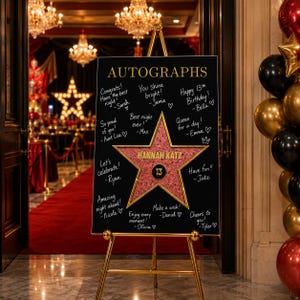 Può includere: Una lavagna rettangolare nera per autografi su un cavalletto dorato con la scritta AUTOGRAPHS in alto e una grande stella centrale glitterata rosa con il nome HANNAH KATZ e il numero 13, circondata da messaggi bianchi scritti a mano.
