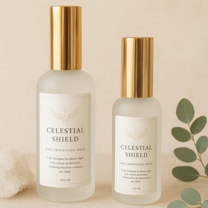 Può includere: Due flaconi spray in vetro smerigliato con tappi color oro. I flaconi hanno etichette bianche con il testo "CELESTIAL SHIELD" e "AURA PROTECTION SPRAY". I flaconi sono da 100 ml ciascuno.