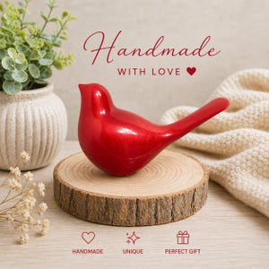 May include: A glossy red bird figurine with a long tail, perched on a wooden slice. The words "Handmade with Love" are written in cursive script above the bird. The image also includes a small plant in a white vase and the words "Handmade", "Unique", and "Perfect Gift".