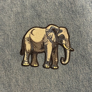 May include: Embroidered elephant patch in shades of tan, brown, and gray, with a black outline. The elephant has a curved trunk and tusks. The patch is on a blue denim background.
