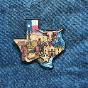 May include: A Texas-shaped embroidered patch featuring a scene with a longhorn, a cowboy on horseback, a windmill, a cowboy hat, a boot, the Alamo, and a star. The top corner displays the Texas flag with a white star on a blue and red background.