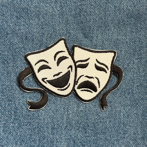 May include: Embroidered patch featuring the classic comedy and tragedy theater masks. The masks are white with black outlines and details, including the smiling and frowning mouths. The patch has a black border and is set against a blue denim background.