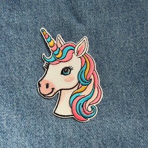 May include: Embroidered unicorn patch featuring a white face, pink cheeks, and a colorful mane and horn. The patch has a black outline and is set against a blue denim background. The unicorn's mane includes shades of pink, blue, and yellow.