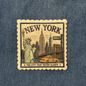 May include: A rectangular embroidered patch with a scalloped edge featuring the Statue of Liberty, the New York City skyline, a yellow taxi, and a Wall Street sign. The text reads NEW YORK and THE CITY THAT NEVER SLEEPS in dark lettering.