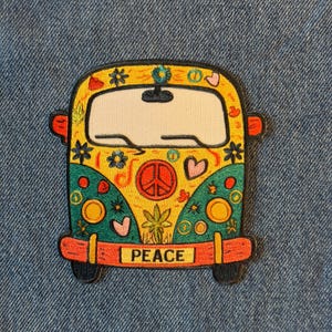 May include: A colorful patch featuring a cartoon-style van with a peace sign, flowers, and hearts. The van is yellow, green, and orange with the word "PEACE" on the front bumper. The patch is likely for clothing or accessories.
