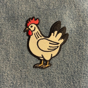 May include: Embroidered patch of a white chicken with black and yellow accents. The chicken has a red comb and wattle. The patch is on a blue denim background. This patch is perfect for adding to clothing or accessories.