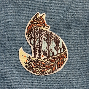May include: Embroidered patch in the shape of a fox, featuring a forest scene within its silhouette. The fox is outlined in white, with details in brown, orange, and light blue. The patch is set against a blue denim background.