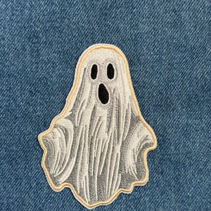 May include: Embroidered ghost patch with a white body, black eyes and mouth, and a tan border. The ghost has a flowing, draped appearance. Perfect for Halloween or spooky-themed crafts.