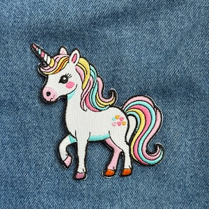 May include: Embroidered unicorn patch with a white body, a rainbow mane and tail, and a spiraled horn. The unicorn has pink cheeks and hooves, and is set against a blue denim background.