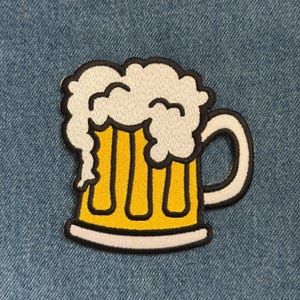 May include: Embroidered patch featuring a yellow beer mug with white foam and a white handle. The patch has a black border and is set against a blue denim background. A fun accessory for clothing or bags.