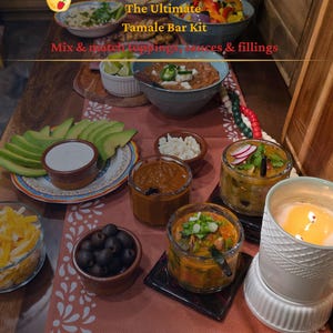 Könnte beinhalten: Eine Tischdekoration mit einer Auswahl an Zutaten für eine Tamale-Bar. Schalen mit Toppings, Saucen und Füllungen sind um Avocado-Scheiben, Oliven und Käse angeordnet. Der Text "Un-Stuffed Tamales, The Ultimate Tamale Bar Kit" ist sichtbar.
