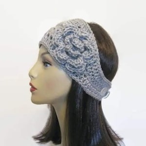 May include: A gray crocheted headband with a floral design. The headband is made of a soft yarn and features a button closure. The floral design is centered on the headband and adds a decorative touch. This accessory is perfect for keeping hair out of the face.