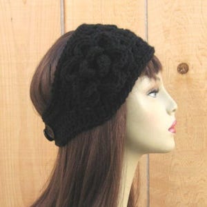 May include: A black crocheted headband with a textured floral design. The headband is secured with a button on the side. The accessory is worn on a person with brown hair.