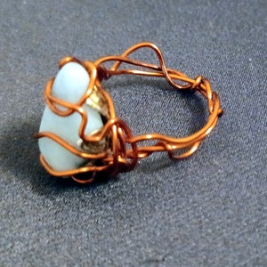 May include: A copper wire ring with a white stone set in the center. The wire is wrapped around the stone in a decorative pattern.