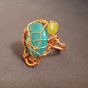 May include: A turquoise gemstone ring with a copper wire design. The ring also features a smaller, yellow gemstone.